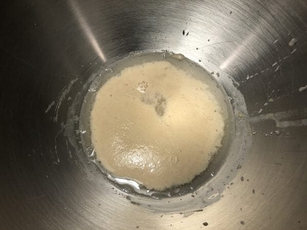 A close-up of yeast mixture foaming in a stainless steel mixing bowl.