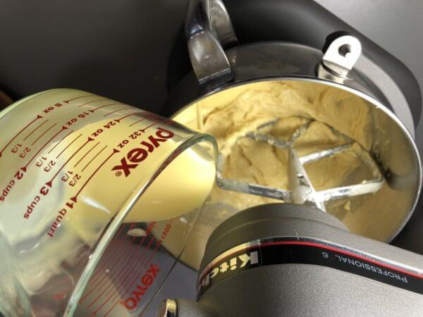 A Pyrex measuring cup pouring batter into a KitchenAid stand mixer bowl.