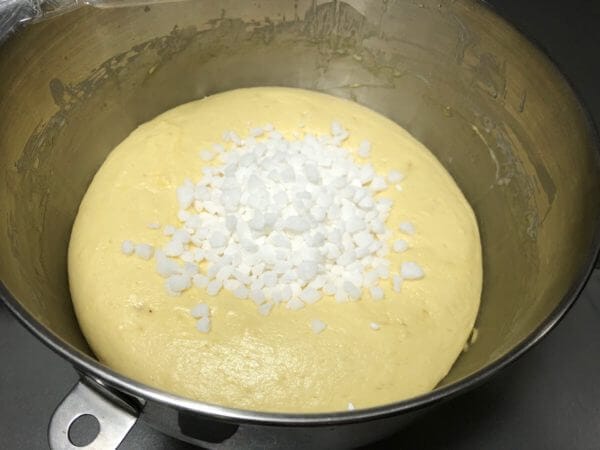 A stainless steel mixing bowl with dough topped with Belgian pearl sugar.
