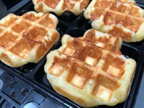Freshly cooked waffles on a waffle iron, golden brown and slightly crispy.