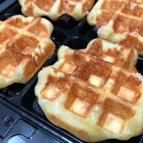 A plate piled high with freshly cooked, golden brown waffles.