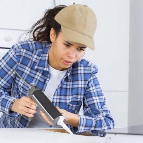 a female laying down a line of caulk to set her sink with.