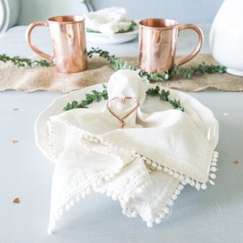 a table setting with a diy copper wire heart napkin holder