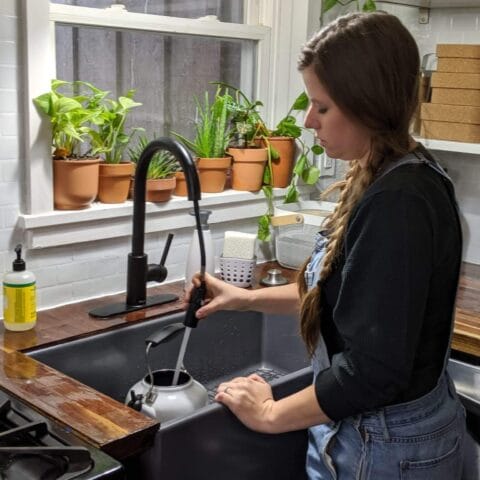 a woman filling up a tea kettle in her gray fireclay kitchen sink.