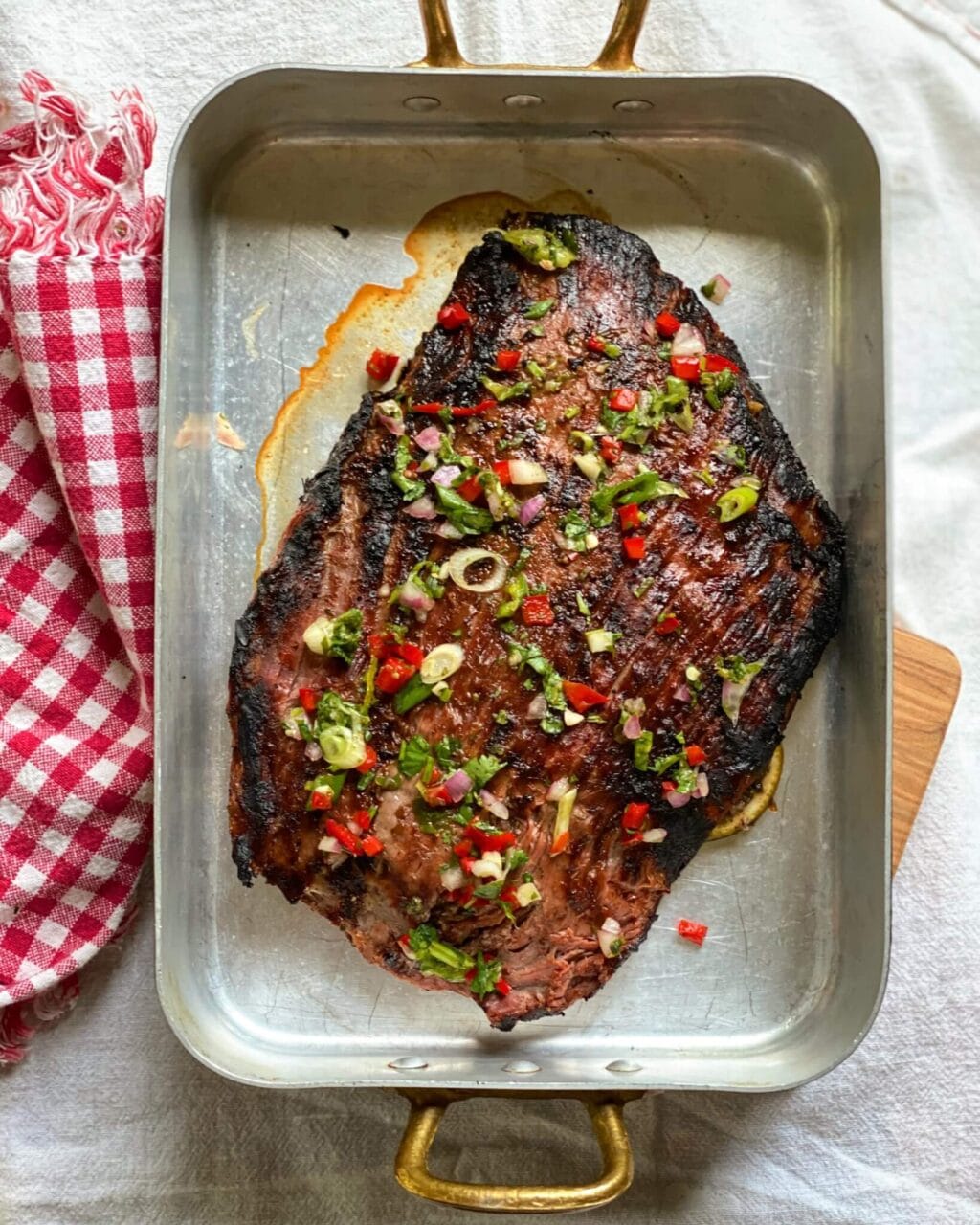 A grilled piece of meat in a baking dish, garnished with chopped vegetables and herbs.