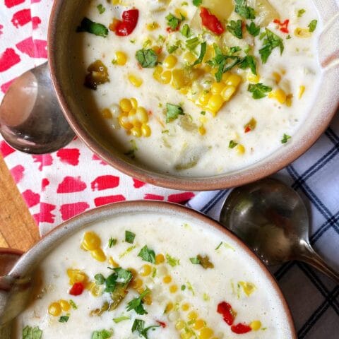 Two bowls of creamy corn chowder garnished with fresh herbs and diced red peppers.