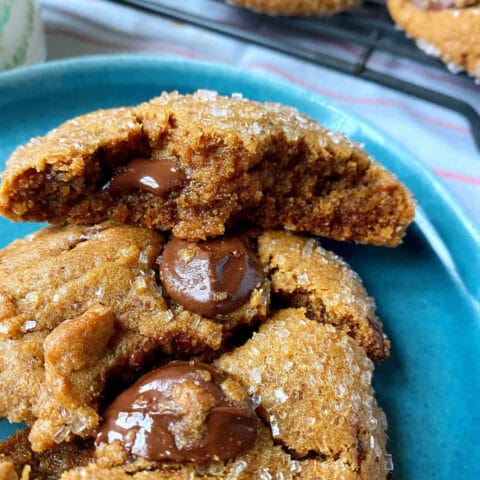 Close-up of a freshly baked chocolate chip cookie on a blue plate, with melty chocolate chips and a sprinkling of sugar on top.