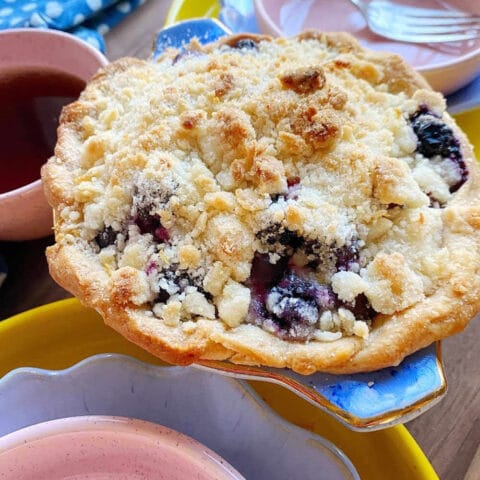 A baked crumble pie with a golden brown topping, featuring blueberries, lemon, and rosemary, with the text "crumble pie blueberry + lemon + rosemary www.sinkology.com" on the image.