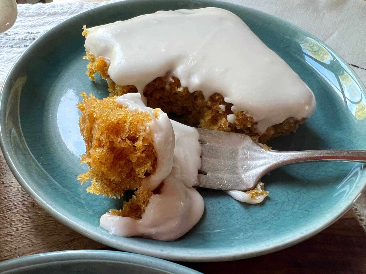 A slice of cake with white frosting on a blue plate, with a fork taking a bite.
