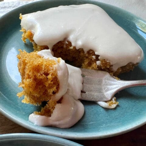 A slice of cake with white frosting on a blue plate, with a fork taking a bite.