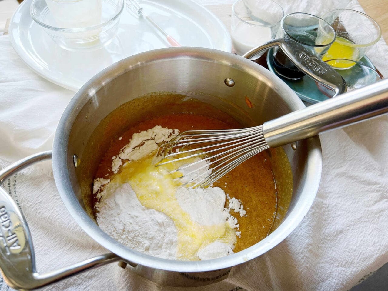 Flour and melted butter being whisked into a pumpkin mixture in a pot.