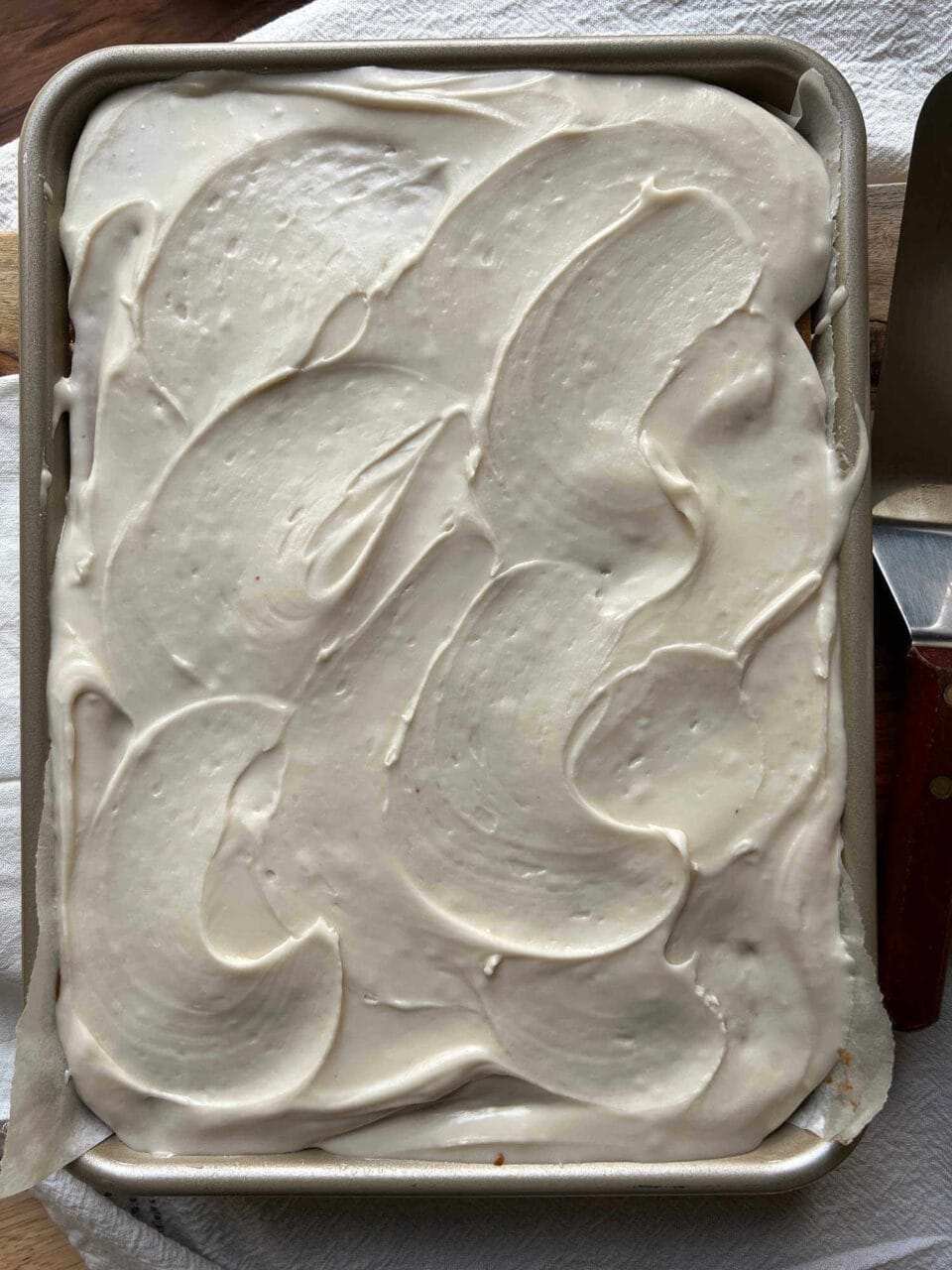 A rectangular cake fully covered with smooth white frosting in a baking pan.