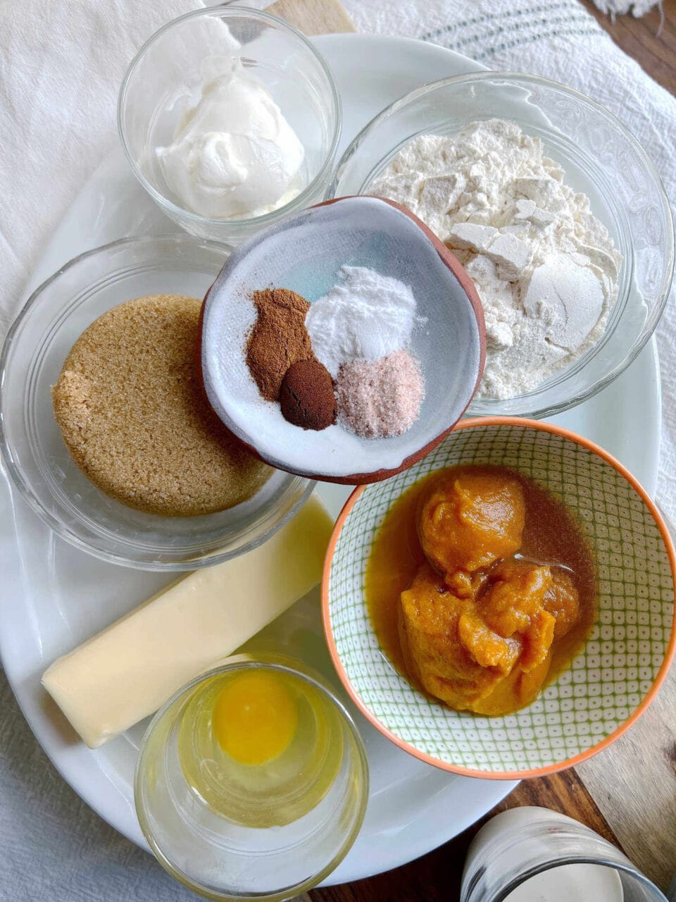 Ingredients for cake, including brown sugar, flour, butter, egg, pumpkin puree, spices, sour cream, and baking powder, arranged on a white plate.