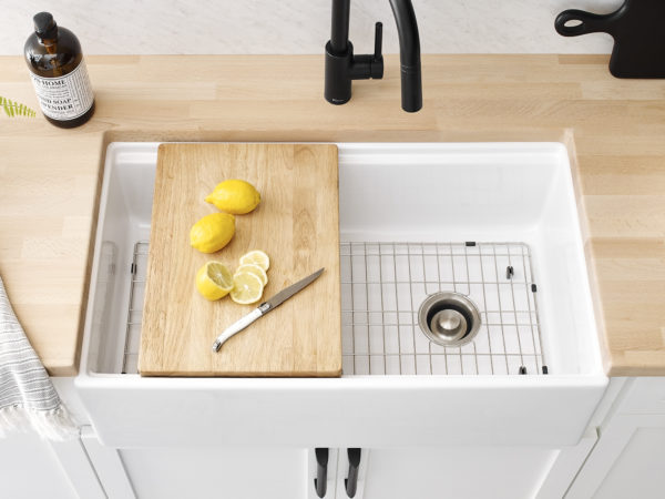 White fireclay farmhouse kitchen sink with cutting board and metal bottom grid