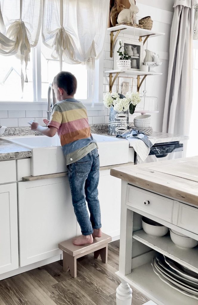 small child standing on a stool cleaning dishes in a fireclay kitchen sink.