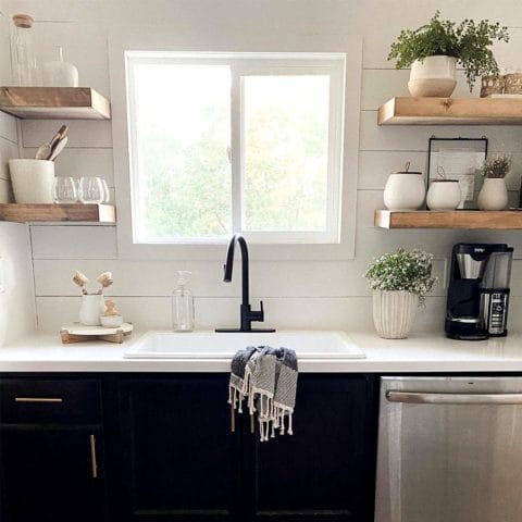 A white drop-in fireclay sink with matching shiplap backsplash and black cabinets