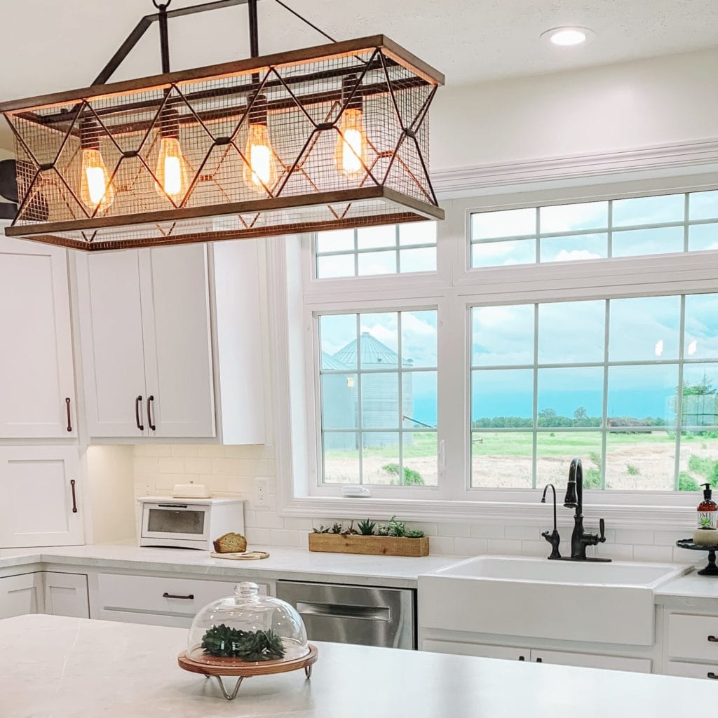 A glossy white rectangular Quick-Fit® drop-in farmhouse sink under a large window in a white kitchen overlooking a mountain range.