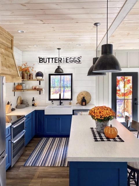 A glossy white rectangular Quick-Fit® drop-in farmhouse sink in the center of a bohemian designed kitchen with blue cabinets and white shiplap walls.