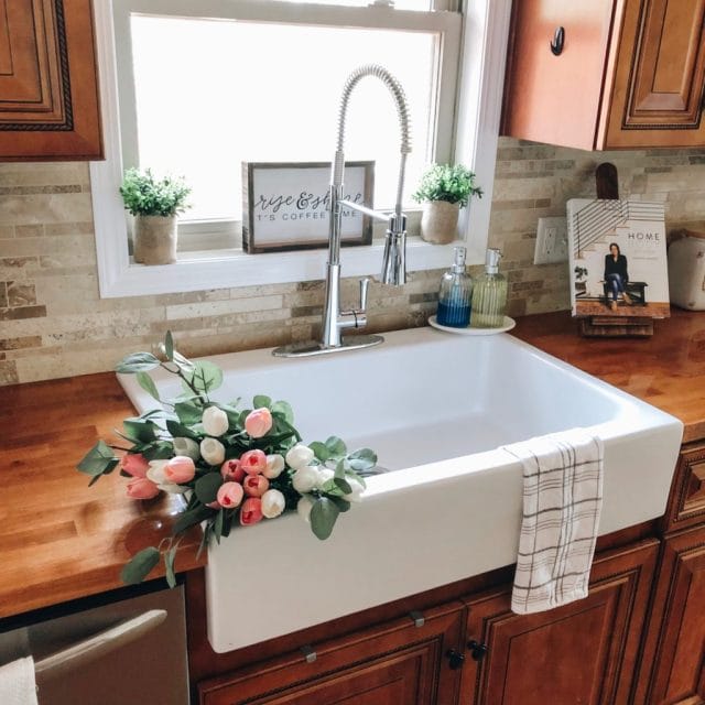 A glossy white rectangular Quick-Fit® drop-in farmhouse sink with chrome pull-down faucet with colorful flowers in the basin.
