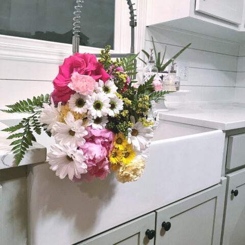 White fireclay farmhouse double bowl kitchen sink with large bouquet of colorful flowers in it