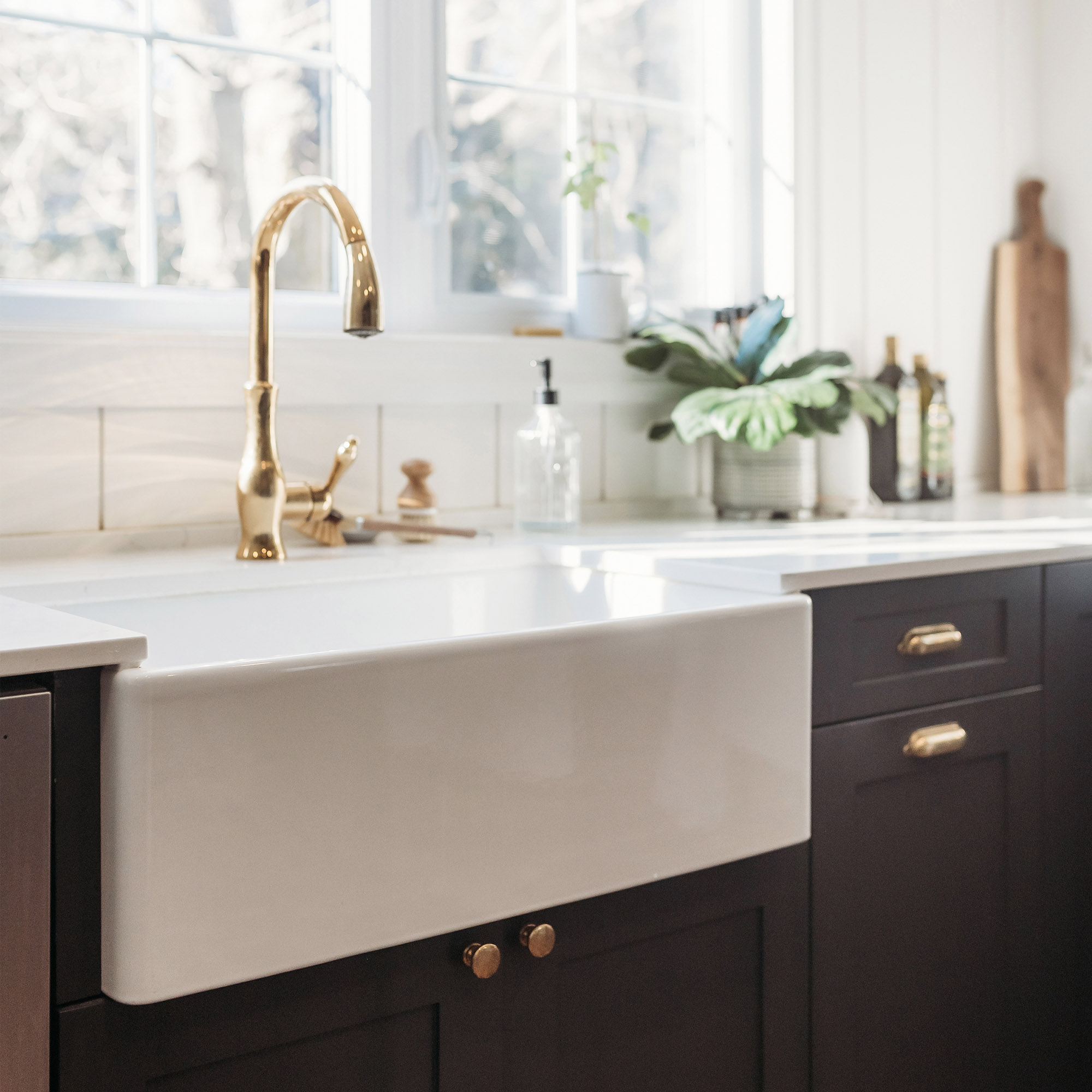 Bright sunlit kitchen with white farmhouse sink and dark gray cabinets.