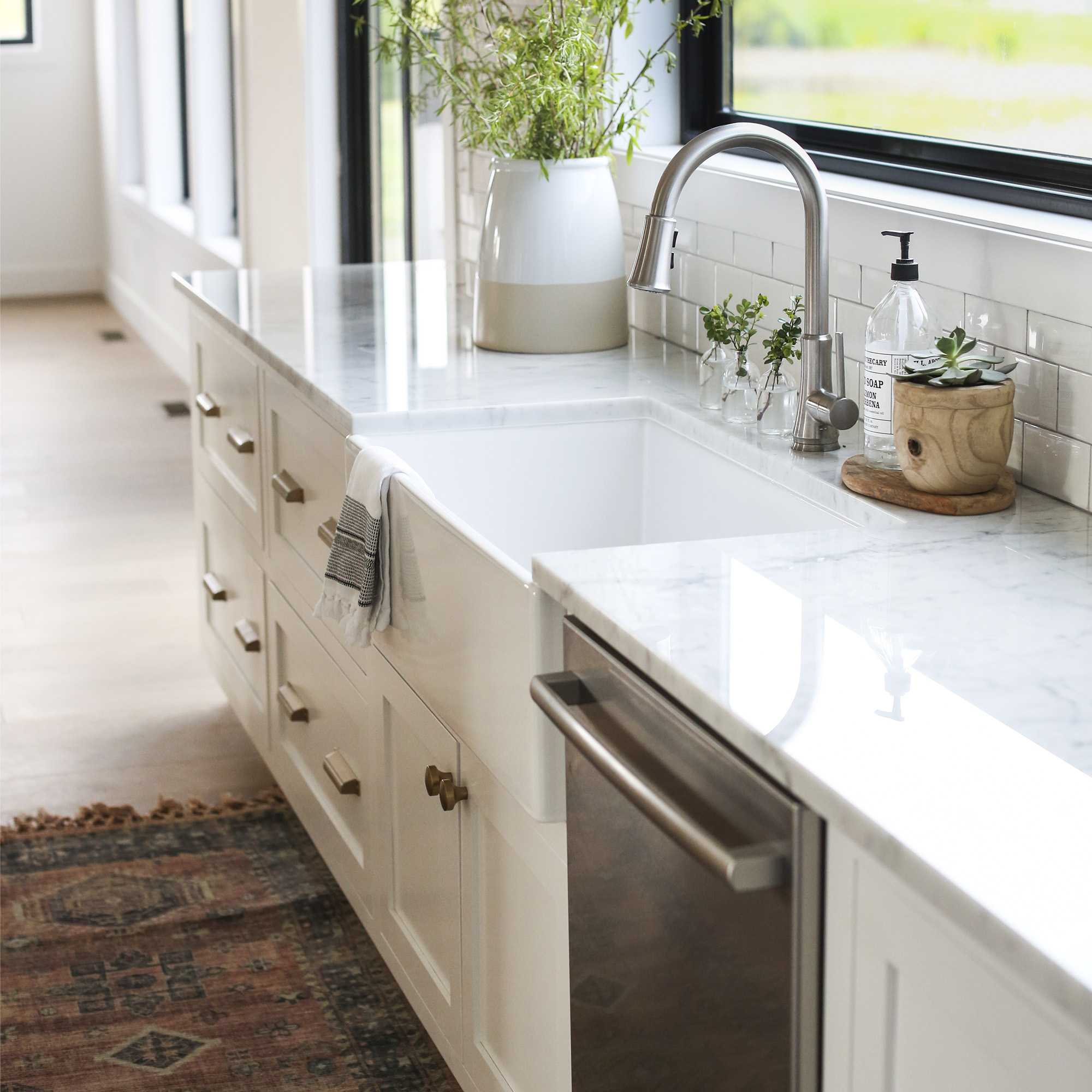 White farmhouse kitchen sink with a brushed nickel faucet in front of a window