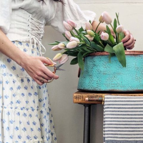 Woman cutting tulips over a round copper vessel bath sink.