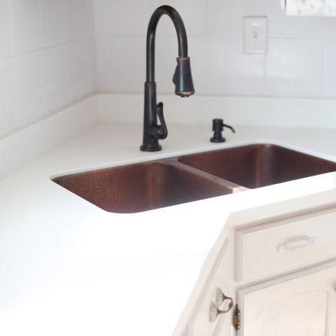 A copper rectangular undermount double basin sink in a home kitchen with a white countertop.