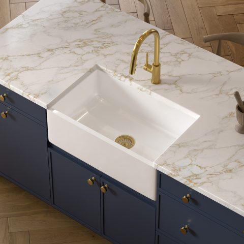 A kitchen with a glossy white rectangular undermount farmhouse sink made in fireclay, set in a marble countertop with a brushed gold pull-down faucet and blue cabinets.