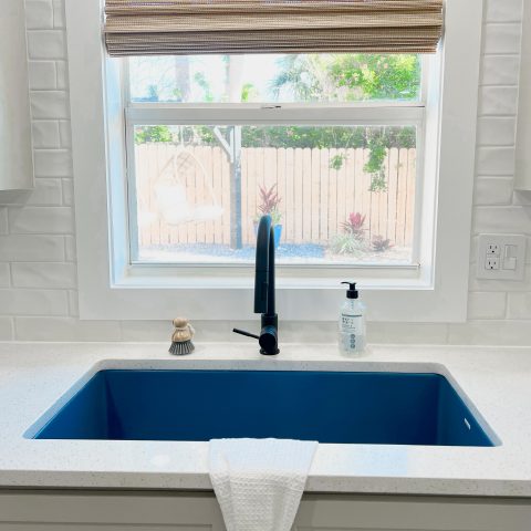 Matte blue undermount fireclay kitchen sink with black faucet in front of a large window.