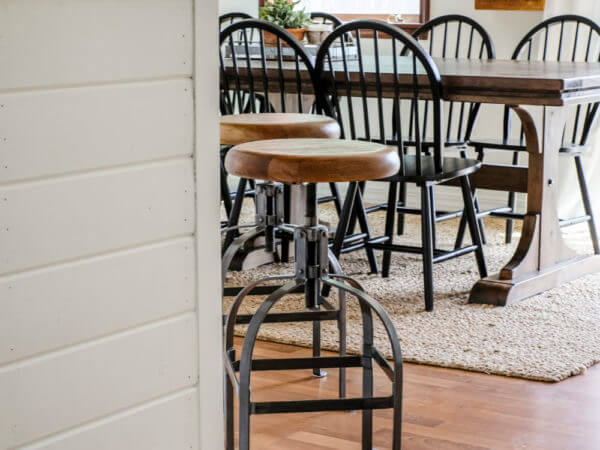 Close-up of a barstool in a kitchen with a view of a dining area featuring a wooden table and black chairs.