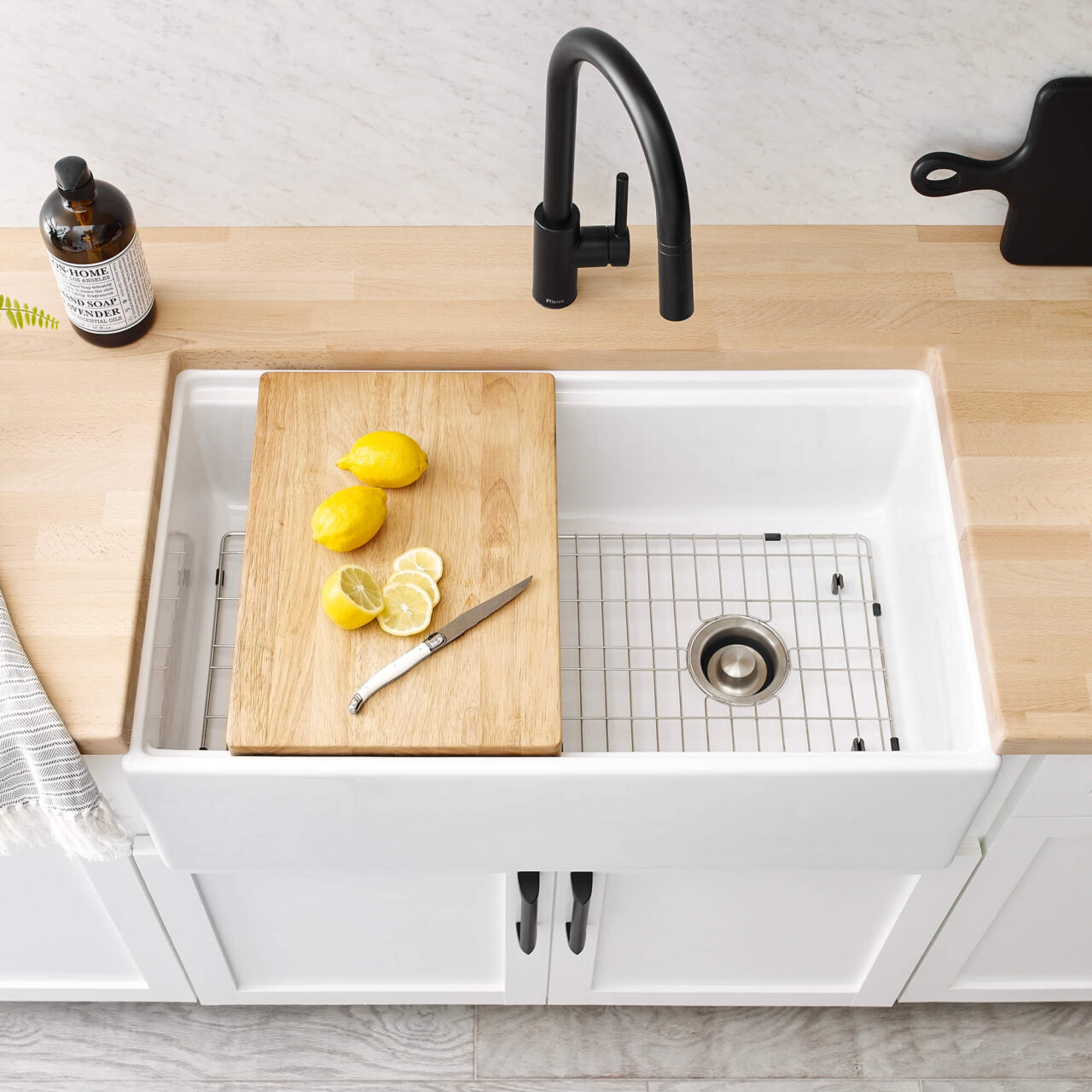 Overhead photo of white rectangular fireclay farmhouse workstation sink with cutting board, bottom grid and matte black faucet with butcher block countertops.