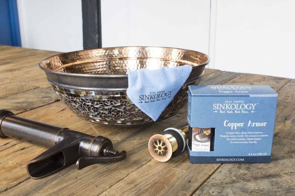 A kitchen sink area with a hammered copper sink, a dark faucet, a large window with a snowy view, and a small plant on the white countertop. A wooden cutting board is in the corner.