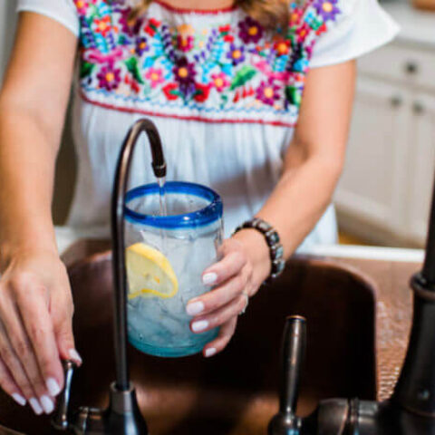 a woman filling up a glass from her copper kitchen sink.