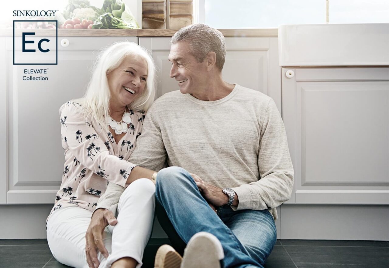 An older couple sitting on the kitchen floor with a "Sinkology Elevate Collection" logo in the top left corner.