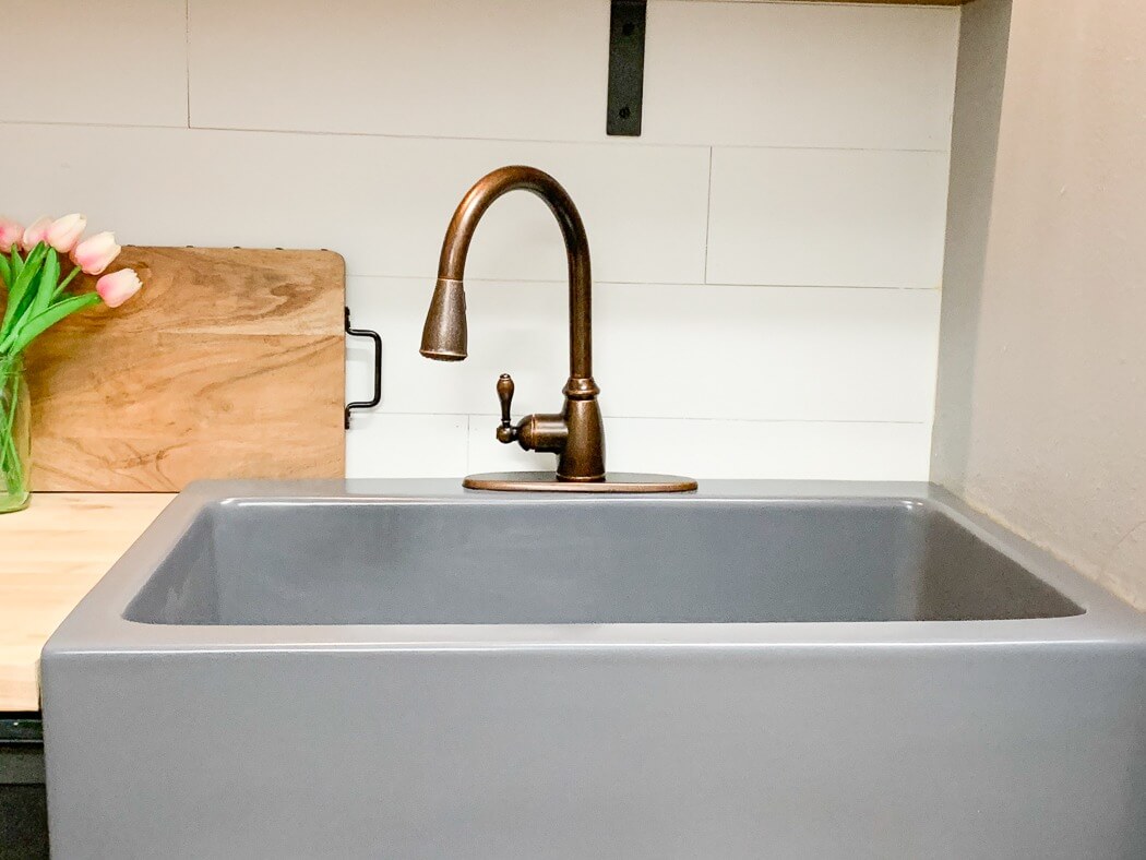 Newly installed gray kitchen sink with a bronze faucet, wooden countertop, and a vase of pink tulips beside a cutting board.