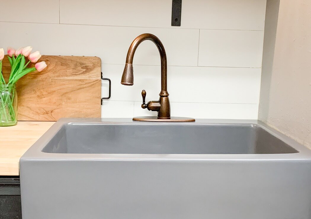 Close-up of a gray kitchen sink with a bronze faucet, a wooden cutting board, and a vase of pink tulips on the counter.