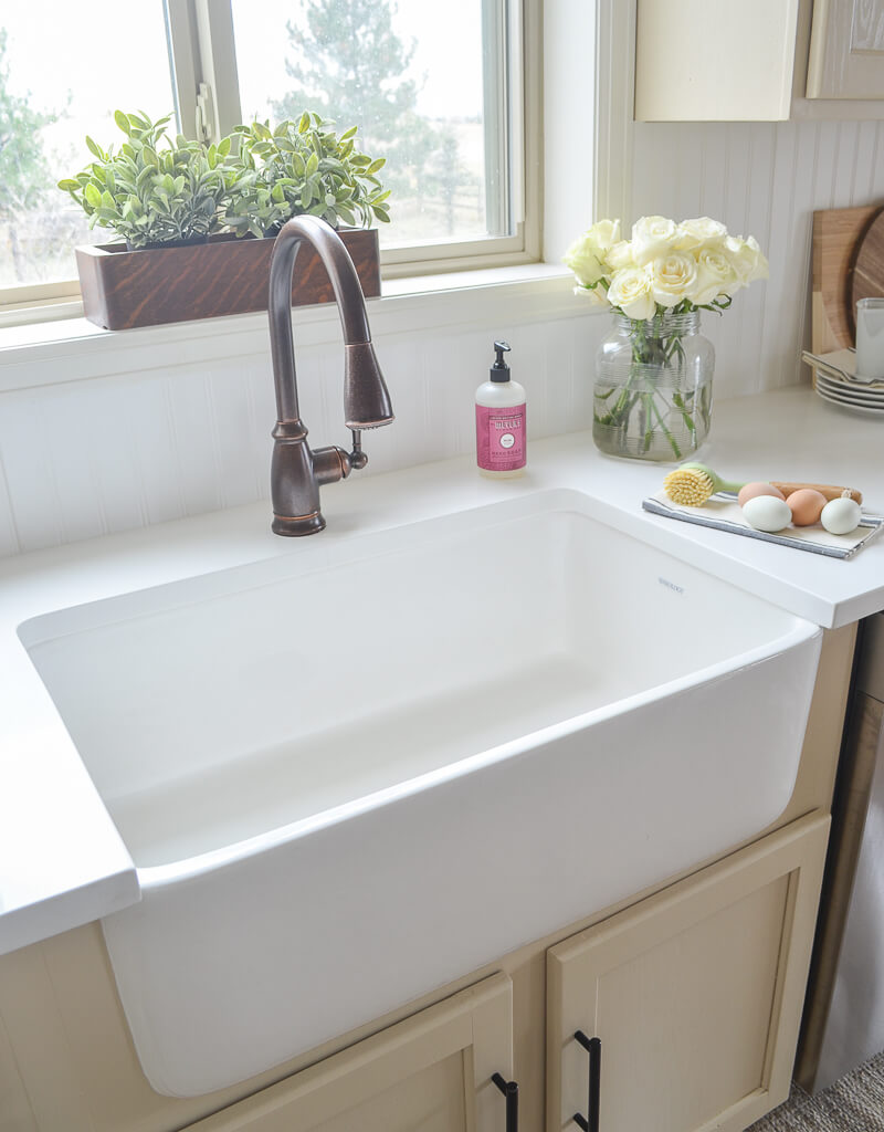 A farmhouse kitchen sink with a bronze faucet, white countertop.