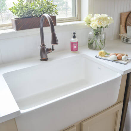 A farmhouse kitchen sink with a bronze faucet, cream cabinets, and a counter.