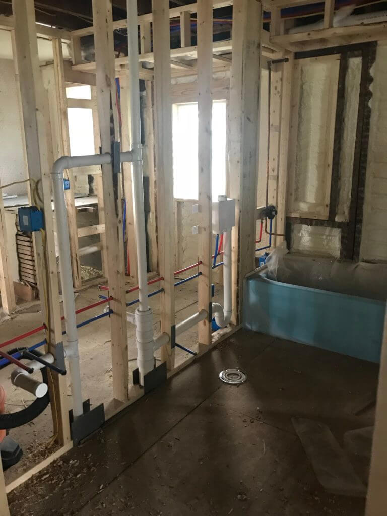 Bathroom under construction with exposed framing and plumbing, featuring a blue bathtub.