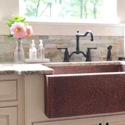 a copper kitchen apron front style sink with pink flowers on the kitchen counter