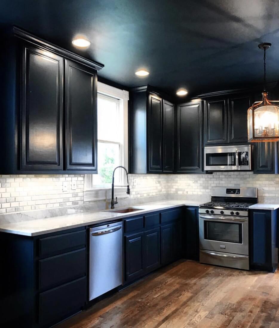 Modern kitchen with dark cabinets, stainless steel appliances, a marble countertop, and a subway tile backsplash, featuring a wood floor and under-cabinet lighting.