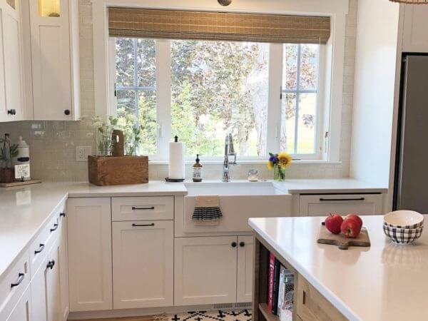 A bright kitchen with white cabinets and a large window above the farmhouse sink.
