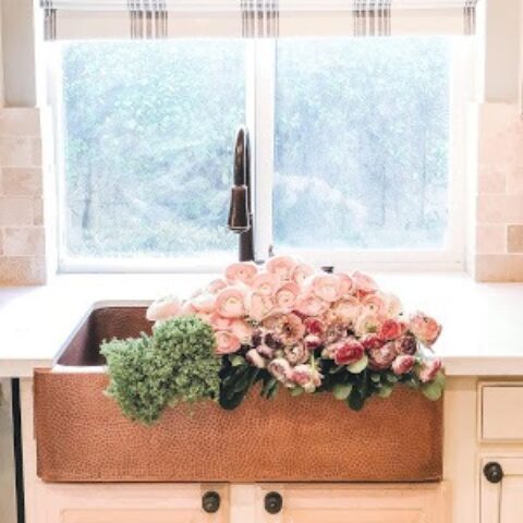 a copper farmhouse sink full of pink flowers