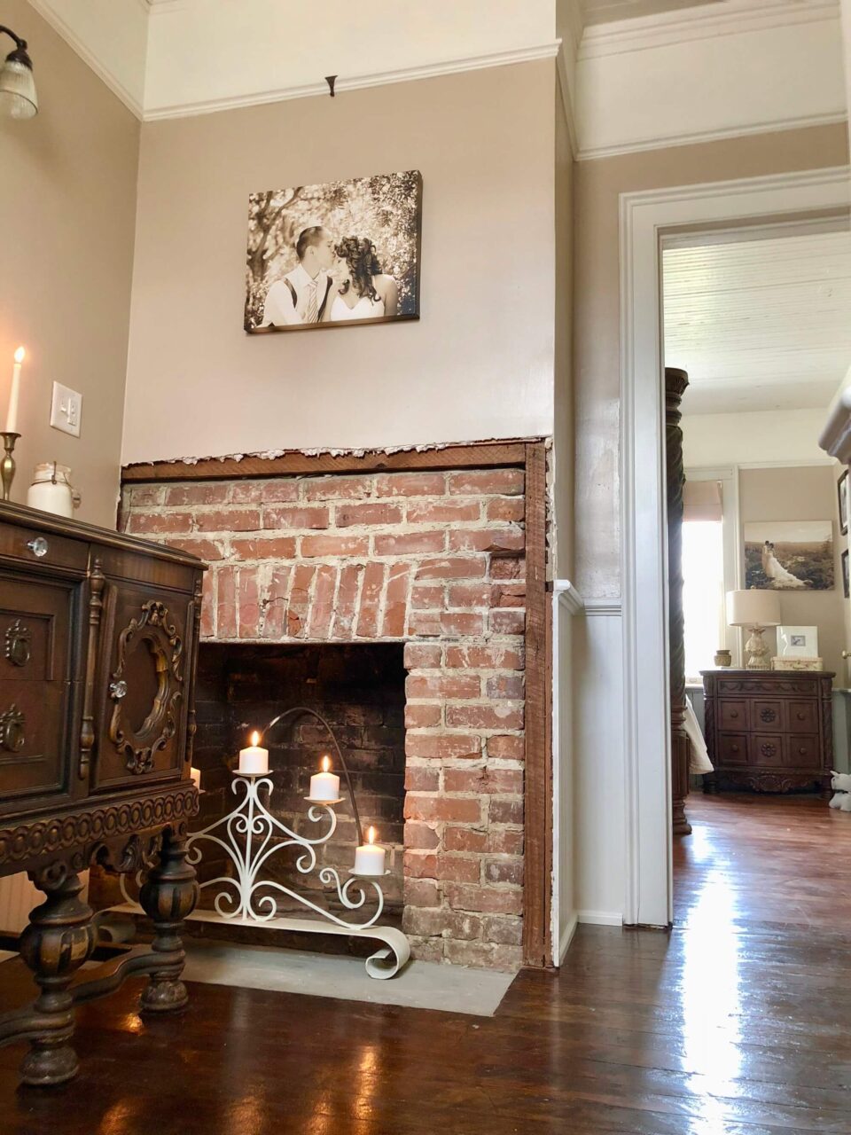 A bathroom with an exposed brick fireplace, a vintage wood vanity, and a decorative candle holder, featuring a sepia-toned photo of a couple on the wall.
