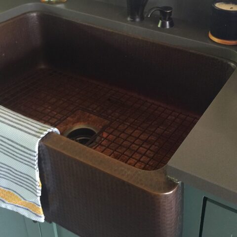 a copper sink with a kitchen towel hanging from the apron front