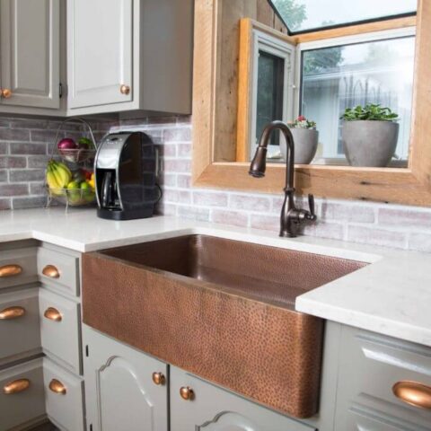 a copper farmhouse sink in kitchen with gray cabinets