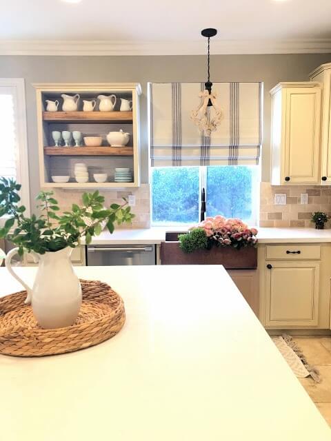 Bright kitchen with cream cabinets, a copper sink, and a large island with a decorative tray.