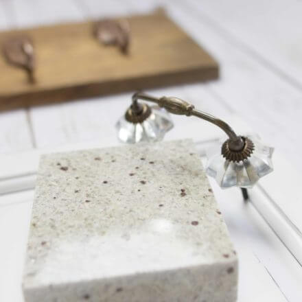 Close-up of a decorative stone object with vintage-style glass and metal accents, placed on a white tray, with a wooden rack featuring bronze feather hooks in the background.