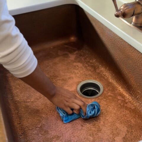 copper kitchen sink with patina being wiped down with rag